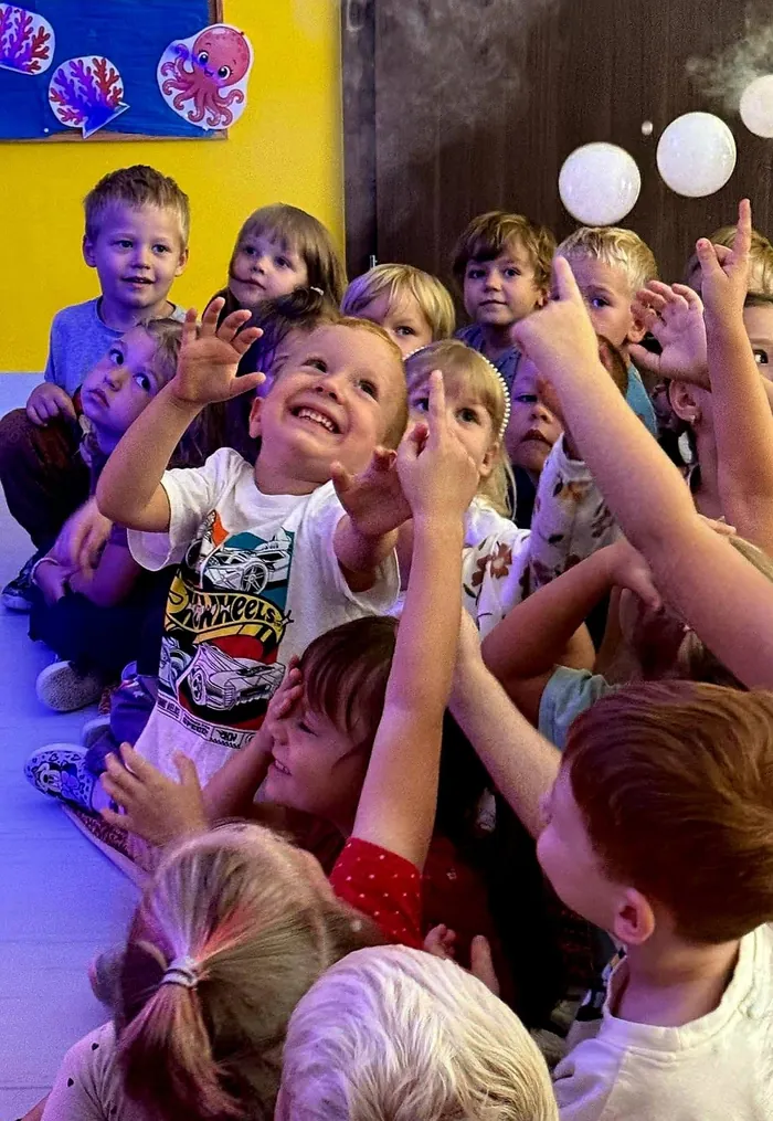 Dzieci wyciągają ręce po białe bańki pełne dymu